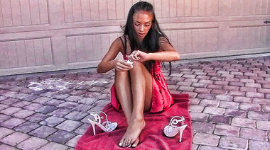 Девушка в платье сидит посреди улицы и смазывает ножки кремом